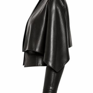 A profile view of a black genuine leather cape jacket featuring a draped asymmetric overlay and a long sleeve against a plain white background.