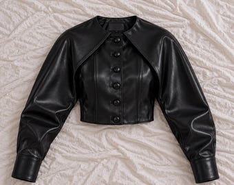 Chaqueta corta de piel auténtica negra, con superposición de hombros tipo capa y cierre de botones en la parte delantera.