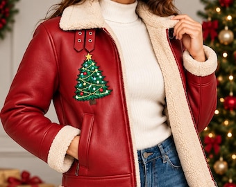 Puede incluir: Una chaqueta de piel sintética roja con forro de sherpa color crema, que presenta un parche bordado de un árbol de Navidad en el pecho, cuello ancho, mangas largas con puños de sherpa y un cierre de cremallera frontal completo.