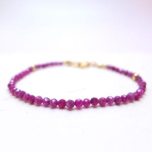 Op de afbeelding: Een delicate armband met kleine, gefacetteerde, dieproze robijnkralen die aan elkaar zijn geregen. De armband heeft goudkleurige accenten en een sluiting. De kralen hebben een diameter van ongeveer 0,3 cm.