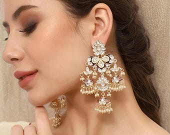 May include: Gold-toned chandelier earrings with a floral design. The earrings feature clear crystals, white pearls, and red and black enamel accents. The earrings have a dangling, tiered design.