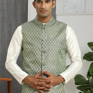 May include: A green and gold patterned vest with a mandarin collar and button closure. The vest is worn over a white long-sleeved shirt. The overall style is traditional and formal.
