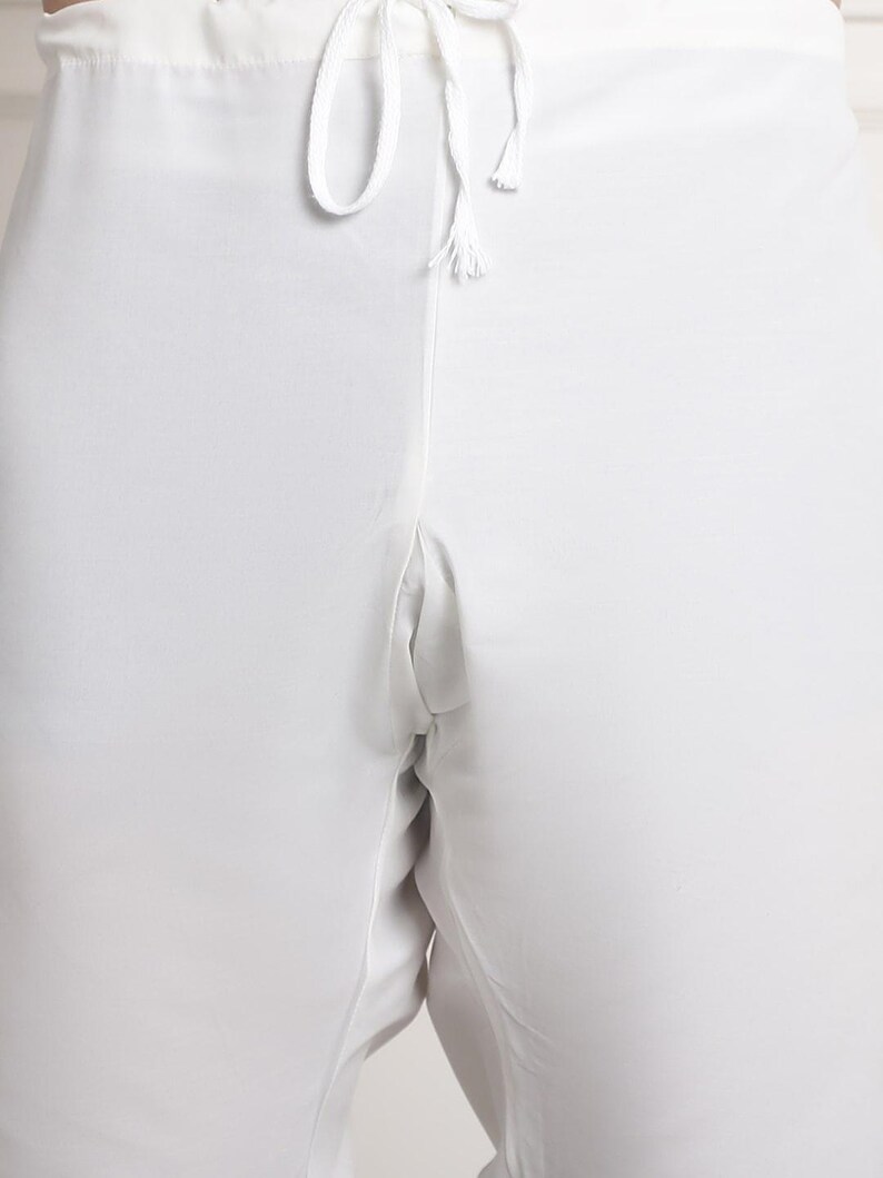 May include: Close-up of white pants with a drawstring waist. The pants are made of a lightweight fabric and have a relaxed fit. The drawstring is white and has a knotted end.