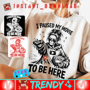 Puede incluir: Una sudadera blanca con un gráfico en blanco y negro de un esqueleto sosteniendo un mando a distancia y palomitas de maíz, con el texto "I PAUSED MY MOVIE TO BE HERE." Incluye dos gráficos más pequeños con el mismo diseño. La palabra "TRENDY" está abajo.