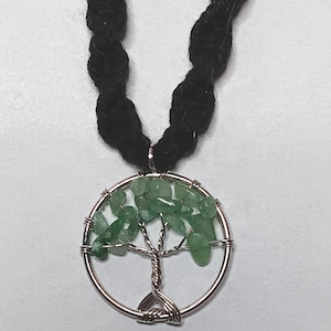 May include: A silver-toned pendant necklace featuring a tree of life design. The tree is crafted with wire and adorned with green gemstone chips, set within a circular frame. The necklace has a black, braided cord.