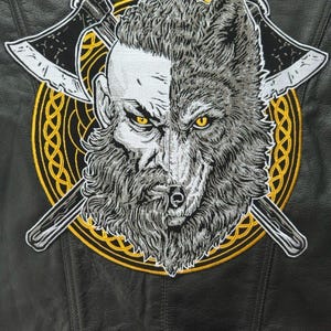 May include: A black leather jacket featuring a large embroidered patch on the back. The patch displays a split-face design of a bearded human and a wolf with yellow eyes, set against a gold circular knotwork border and two crossed axes.