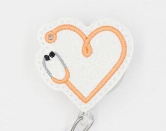 May include: White glitter heart-shaped badge holder with an orange stethoscope design. The badge holder has a clear plastic clip.