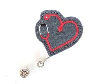 May include: A gray felt heart with a red embroidered stethoscope design. The heart is attached to a clear plastic retractable badge holder.
