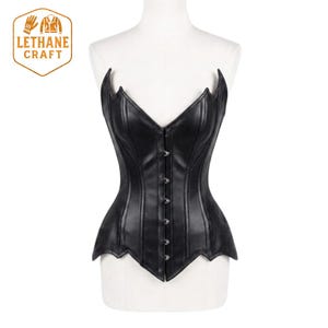 May include: A black corset featuring a pointed bat-wing neckline and a vertical front closure with silver-toned metal clasps. The garment is constructed with structured vertical seams and a scalloped hemline, displayed on a white mannequin.