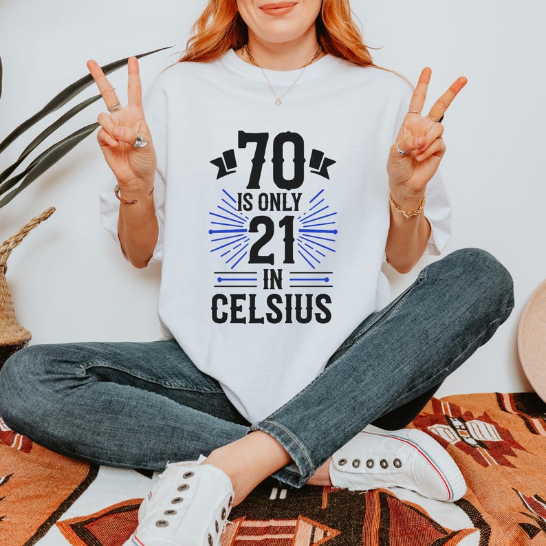 以下が含まれることがあります： 白地に「70 is only 21 in Celsius」の文字が黒と青でプリントされたTシャツ。カジュアルなスタイルで、普段使いに適しています。年齢を遊び心で表現したデザインです。