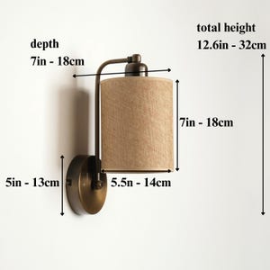 May include: A wall-mounted lamp with a bronze finish and a cylindrical lampshade. The lampshade is beige and has dimensions of 7 inches to 18 inches. The total height is 12.6 inches to 32 cm. The depth is 7 inches to 18 cm.