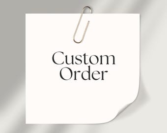 May include: A white square sticky note with the words "Custom Order" in black script is held by a silver paper clip. The bottom right corner of the note is curled up. The background is a light gray.