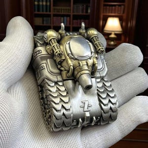 Può includere: Un accendino a forma di carro armato argentato e dettagliato con accenti dorati. Il carro armato in miniatura presenta intricati dettagli meccanici, tra cui torrette, cingoli e un cannone anteriore. L'accendino è tenuto in una mano guantata.