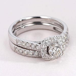 May include: A diamond engagement ring set with a round central stone and a halo of smaller diamonds. The band is also encrusted with diamonds. The ring is set in a white metal, likely platinum or white gold.