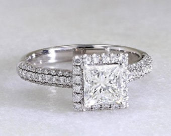 May include: A diamond engagement ring with a square-cut center stone, surrounded by a halo of smaller diamonds. The band is also encrusted with diamonds, creating a sparkling effect. The ring is set in a white metal, likely platinum or white gold.