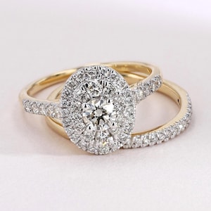 May include: A set of two rings, a wedding and engagement ring, with a gold band. The engagement ring features a large, oval-cut diamond surrounded by a halo of smaller diamonds. The wedding band is also adorned with small diamonds.