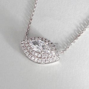 May include: A delicate silver necklace featuring a marquise-cut diamond pendant. The diamond is surrounded by a halo of smaller, sparkling stones, creating a brilliant display. The pendant is suspended from a fine chain.