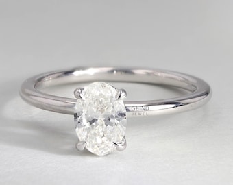 May include: A silver engagement ring with a large, oval-cut diamond as the centerpiece. The diamond is held in place by four prongs, and the band is thin and polished. The ring is set against a neutral background. The text "GLIND JEWEL" is visible.