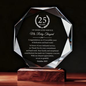 May include: A clear, faceted crystal award with a wooden base. The award commemorates 25 years of dedicated service and includes the name "Mr. Ricky Thagard" and the date "October 2025". The text is in white against a black background.