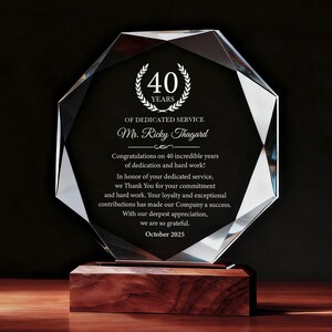 May include: A clear, faceted crystal award on a wooden base. The award displays the text "40 YEARS OF DEDICATED SERVICE" and a personalized message for Mr. Ricky Thagard, celebrating 40 years of service. The date "October 2025" is also included.