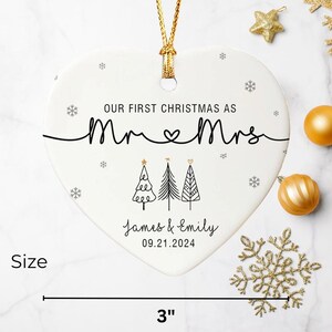 May include: A heart-shaped Christmas ornament with the text "OUR FIRST CHRISTMAS AS Mr & Mrs" and the names "James & Emily" with the date "09.21.2024". The ornament is 3 inches wide and has a gold hanging cord.