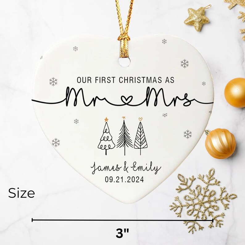 May include: A heart-shaped Christmas ornament with the text "OUR FIRST CHRISTMAS AS Mr & Mrs" and the names "James & Emily" with the date "09.21.2024". The ornament is 3 inches wide and has a gold hanging cord.