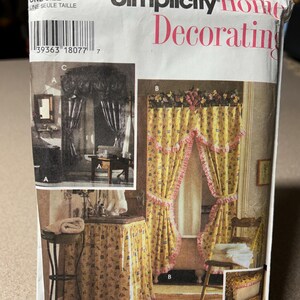 May include: A Simplicity Home Decorating pattern packet. The packet features images of curtains, valances, and a sink skirt. The main image shows yellow curtains with pink trim and floral patterns. The text "Simplicity Home Decorating" is visible.