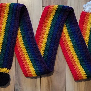 May include: A rainbow crocheted scarf with black and white crocheted pot of gold embellishments at each end.