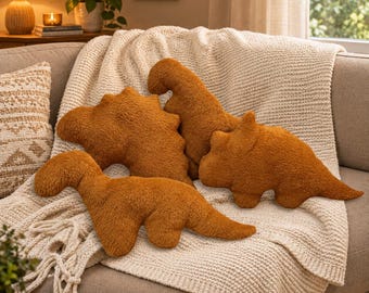 May include: Three plush dinosaur-shaped pillows in a solid burnt orange color. The pillows feature a soft, fuzzy texture and are shaped like different dinosaur species, including a long-necked sauropod, a stegosaurus, and a triceratops silhouette.