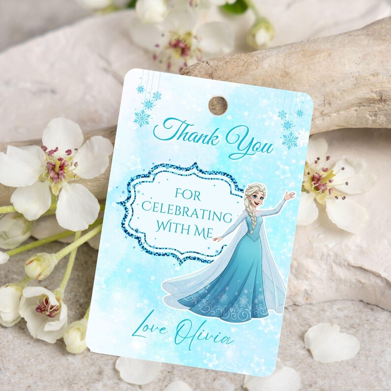 Puede incluir: Una etiqueta de regalo azul claro con el texto "Thank You For Celebrating With Me Love Olivia". La etiqueta presenta una ilustraci&oacute;n de dibujos animados de una princesa con un vestido azul, con un dise&ntilde;o de copo de nieve.