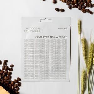 May include: A white packet of hydrogel eye patches with the text "HYDROGEL EYE PATCHES" and "YOUR EYES TELL A STORY". The background includes coffee beans and wheat stalks.