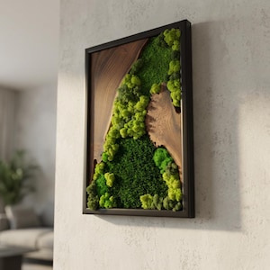 May include: A framed wall art piece featuring a natural design. The artwork combines a dark wood frame with a central section of vibrant green moss and a section of natural wood grain. The moss varies in shades of green, creating a textured, organic appearance.