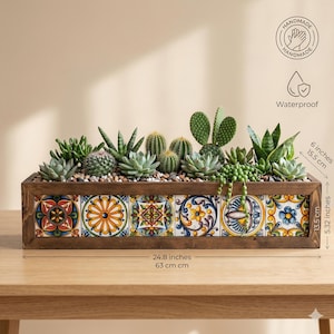 May include: A rectangular wooden planter box featuring six decorative tiles with colorful geometric and floral patterns. The planter contains a variety of green succulents and cacti. It measures 24.8 inches long, 6 inches high, and 5.32 inches deep.