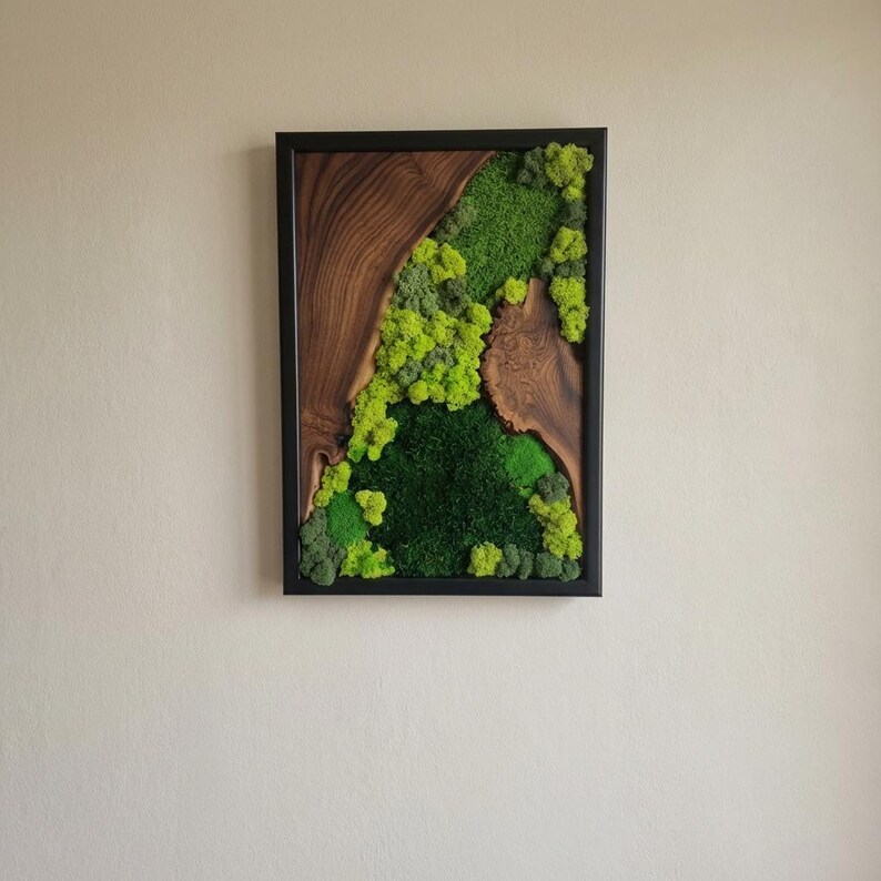 May include: A rectangular wall art piece featuring a natural wood grain design and vibrant green moss. The artwork is framed in a black border, creating a striking contrast between the organic elements and the sleek frame. The moss varies in shades of green.