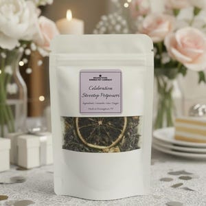 May include: A white pouch of Celebration Stovetop Potpourri with a clear window showing dried ingredients and a slice of citrus. The label lists ingredients and the brand name. The background includes flowers, candles, and a cake.