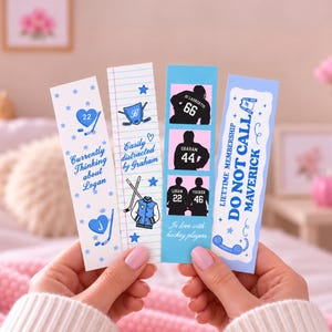 Puede incluir: Cuatro marcapáginas rectangulares de papel con diseños de hockey. Uno presenta corazones azules y el texto "Currently Thinking about Logan". Otro tiene patrones de papel rayado y "Easily distracted by Graham". Un tercero muestra camisetas de hockey, y el último dice "LIFETIME MEMBERSHIP DO NOT CALL MAVERICK" con un icono de teléfono.
