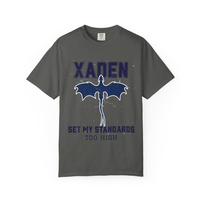 White Comfort Colors tee flat lay Xaden navy dragon graphic tied knot on white bedding, label visible