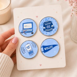 Peut inclure: Un ensemble de quatre pin's circulaires en émail sur une carte de présentation. Les pin's présentent des fonds bleu clair avec des illustrations sur le thème du hockey, dont un ordinateur portable, un maillot bleu Graham 44, un téléphone avec Do Not Call et un fanion bleu avec le texte Wellsy.