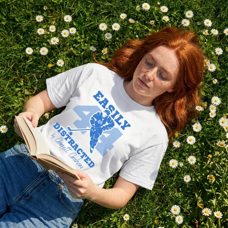 Off Campus t shirt white tee Garrett Graham 44 blue hockey print, redhead model reading book in daisy field