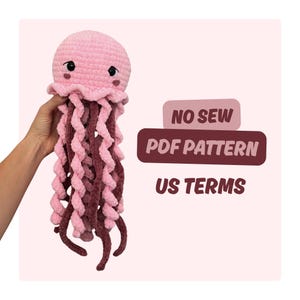 Puede incluir: Un juguete de peluche de medusa hecho a ganchillo con una cabeza redondeada de color rosa claro, mejillas rosa oscuro y largos tentáculos en espiral de hilo rosa claro y oscuro. El texto a la derecha dice NO SEW PDF PATTERN US TERMS.