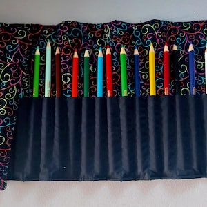 Può includere: Un rotolo per matite in tessuto nero con un motivo a spirale colorato. Il rotolo ha 16 fessure per matite e una patta con chiusura a bottone.