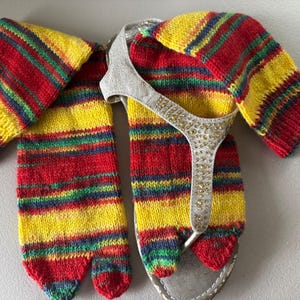 May include: A pair of knitted leg warmers and matching toe socks in red, yellow, green, and blue stripes, paired with silver sandals. The sandals have a silver strap adorned with small, sparkly embellishments.