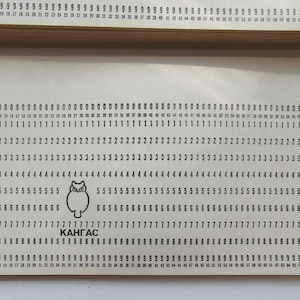 May include: A vintage beige punch card with rows of numbered holes. The card features an owl graphic and the word "KAHГAC". The card is part of a stack of similar cards.