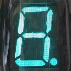 Może przedstawiać: Zabytkowa lampa Nixie wyświetlająca cyfrę 3 w jasnym turkusie. Cyfra jest podświetlona w szklanej obudowie, na tle siatki. Mała kropka jest widoczna po prawej stronie liczby.