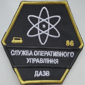 Peut inclure: Écusson brodé noir et or avec un symbole d'atome blanc. Le patch porte le texte "СЛУЖБА ОПЕРАТИВНОГО УПРАВЛІННЯ ДАЗВ" et le numéro "86". L'écusson est de forme hexagonale.