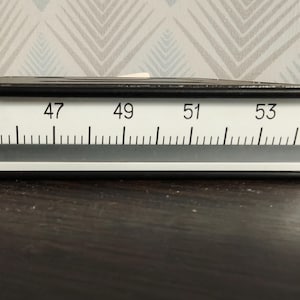 Könnte beinhalten: Ein rechteckiges Frequenzmessgerät mit schwarzem Rahmen und weißem Anzeigefeld. Das Display zeigt den Text Hz, eine horizontale Skala von 45 bis 55 und einen zentralen grauen Balkenindikator. Das Gerät ist für die elektrische Überwachung.