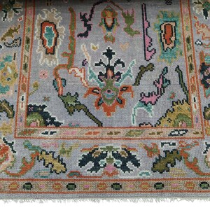 May include: A rectangular, hand-knotted rug with a gray background and a detailed border. The rug features a central design with floral and geometric patterns in shades of orange, green, pink, and blue. The rug has a fringed edge.