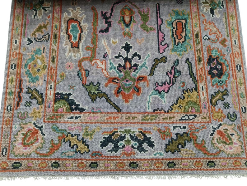 May include: A rectangular, hand-knotted rug with a gray background and a detailed border. The rug features a central design with floral and geometric patterns in shades of orange, green, pink, and blue. The rug has a fringed edge.