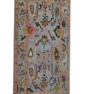 May include: A rectangular, gray rug with an intricate, colorful pattern. The design features floral and geometric shapes in shades of pink, green, orange, and blue. The rug has a detailed border and is likely made of woven material.