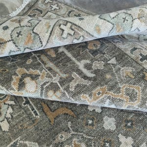 May include: Close-up of a rolled-up area rug with a traditional design. The rug features a color palette of gray, beige, and muted green. The pattern includes floral and geometric elements.